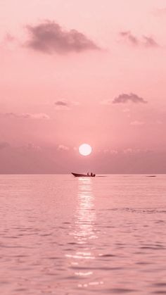 the sun is setting over the ocean with a small boat in the water below it