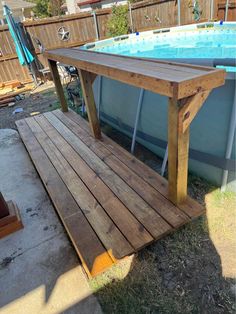 a wooden table sitting next to a swimming pool in a backyard with a bench on the side