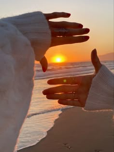 two hands touching each other with the sun setting in the distance behind them, on a beach