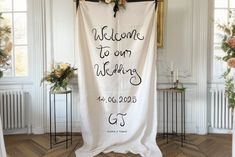 a welcome sign hanging from the side of a wall in a room with floral arrangements