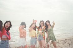 four girls standing on the beach with their arms in the air and one girl holding up her hand