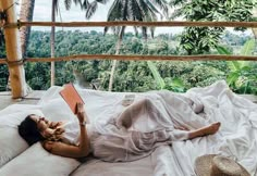 a woman laying on top of a bed next to a lush green forest covered hillside