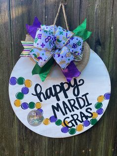 a happy mardi gras sign hanging on a wooden fence with purple and green bows