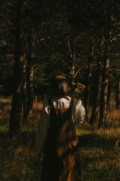 a person standing in the woods holding an object up to their face with both hands