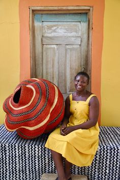 a woman sitting on a bench next to a large red and yellow hat in front of a door