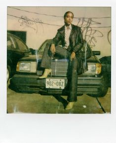 a man sitting on top of a car in front of a wall with graffiti written on it