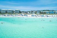 many people are swimming in the clear blue water at an ocean beach with hotels behind them