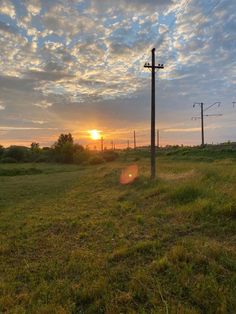 the sun is setting over a field with power lines and telephone poles in the foreground