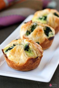 three mini quiches with spinach on a white plate next to a purple pillow