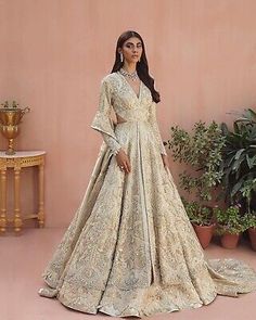 a woman standing in front of a pink wall wearing a white and gold wedding gown