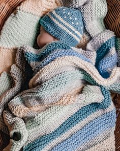 a newborn baby wrapped in a blanket and wearing a knitted hat on top of a wicker basket