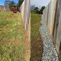 there is a long line of rocks in the grass next to a wooden fence with a red truck behind it