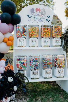 an assortment of candies on display in front of a sign with balloons and decorations