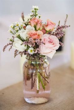 a vase filled with pink and white flowers on top of a wooden table next to candles