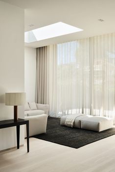 a living room filled with white furniture and windows covered in sheer draping next to a black table