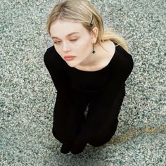 a woman sitting on the ground with her eyes closed and hands behind her head looking down