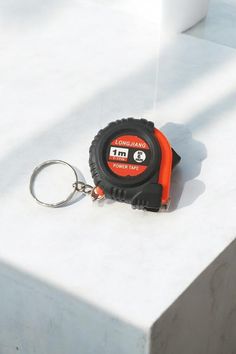 an orange and black tape measure sitting on top of a white table next to a keychain