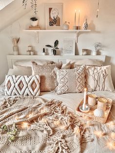 a white bed topped with lots of pillows next to a shelf filled with candles and other items