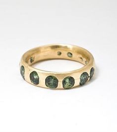 a gold ring with green stones on the inside and outside, sitting on a white surface