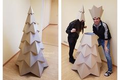 two people standing next to each other near a cardboard christmas tree