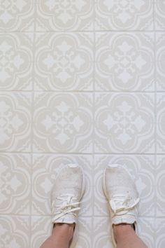 a person's feet with white shoes standing in front of a tile wall and floor