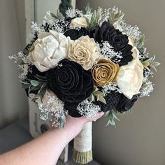 a bridal bouquet with black, white and gold flowers is being held by someone's hand