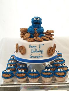 a birthday cake decorated with cookies and cookie monster on top is surrounded by cupcakes