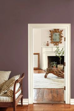 an open door leading to a living room with purple walls and wood flooring in front of a fireplace