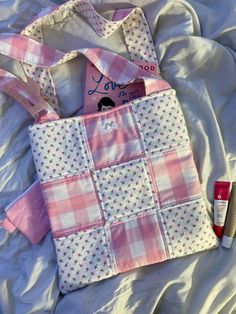 a pink and white bag sitting on top of a bed next to a tube of lipstick