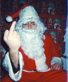 a man dressed as santa clause holding his hands up in front of him with many pictures on the wall behind him