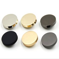 four different colors of round magnets on a white surface with one black, one gold and one silver