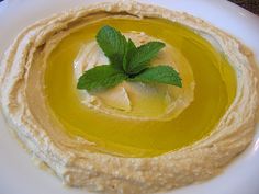 a bowl filled with hummus and topped with a green leaf on the top, sitting on a white plate