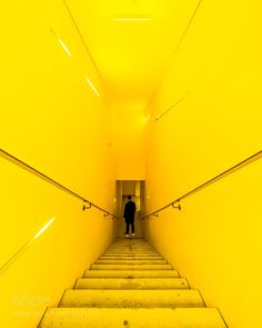 a man is walking up some stairs in a yellow room with bright lights on the ceiling