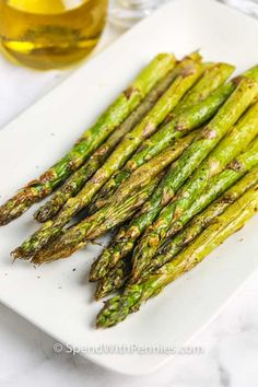 asparagus spears on a white plate next to a glass of oil and pepper