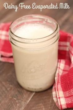 a glass jar filled with milk sitting on top of a wooden table next to a red and white checkered napkin