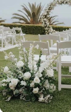 an outdoor ceremony setup with white flowers and greenery on the grass in front of chairs