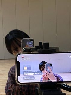 a woman taking a photo with her cell phone while sitting in front of a camera