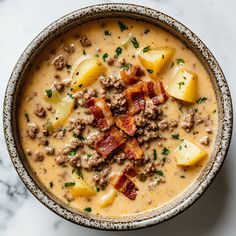 a close up of a bowl of soup with potatoes and meat on top, sitting on a marble surface