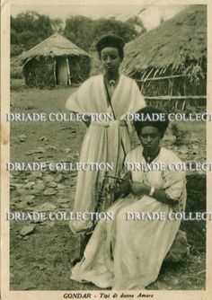 an old black and white photo of two women in front of some huts with thatched roofs