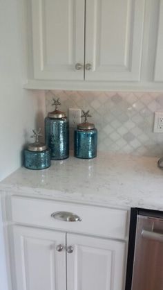 a kitchen with white cabinets and blue jars on the counter top next to a dishwasher