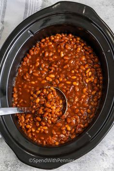 a spoon in a slow cooker filled with baked beans, ready to be cooked