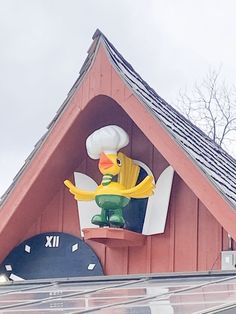 a large rubber duck sitting on top of a roof next to a clock and weather vane