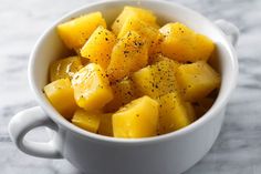 a white bowl filled with sliced pineapple on top of a marble countertop next to a knife