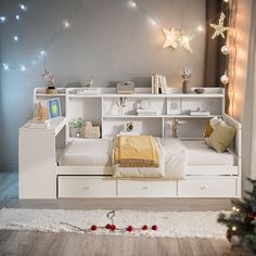 a white bed sitting under a christmas tree next to a wall with lights on it