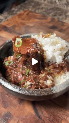 a bowl filled with meat and rice on top of a wooden table