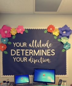 two computer monitors sitting on top of a desk in front of a chalkboard that says your attitude determines your direction