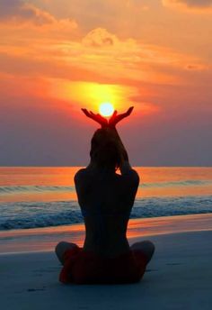 a person sitting on the beach with their hands up in the air as the sun sets