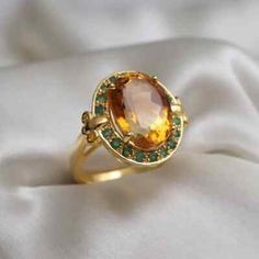 a gold ring with an orange stone surrounded by green and white stones on a white cloth