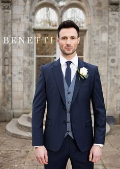 a man wearing a suit and tie standing in front of an old building with the words benefitti written on it