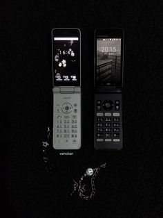 two cell phones sitting next to each other on top of a black surface with chains